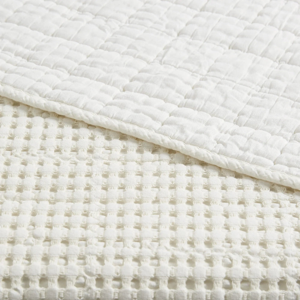 Close-up of a white waffle weave quilt and textured bedding, highlighting the soft fabric and square stitched patterns.