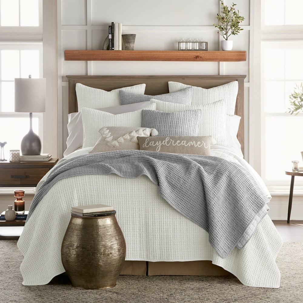 White and grey waffle knit quilt set on a wooden bed with decorative pillows and rustic bedroom decor.