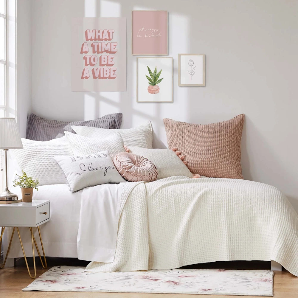 White waffle quilt bed set with pink and grey accent pillows and botanical wall art in a bright, modern bedroom.