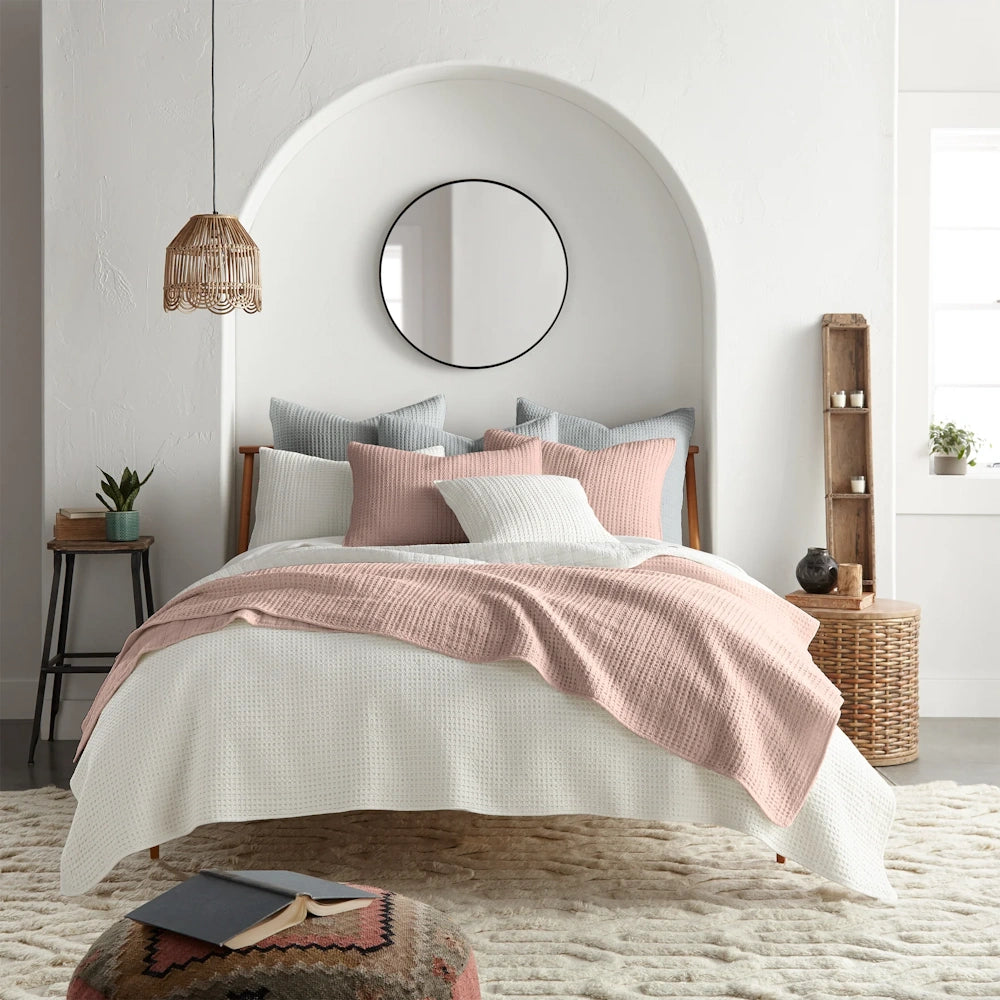 Pink and white waffle weave quilt set on a bed in a modern, boho bedroom with an arched wall nook and round mirror.