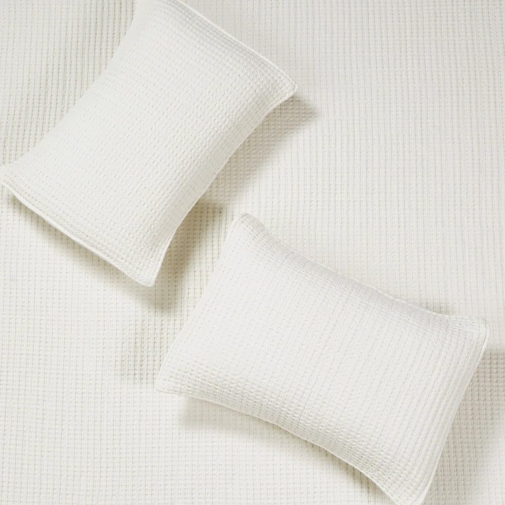 White waffle weave quilt and two matching pillow shams in a clean, minimalist bedroom setting.