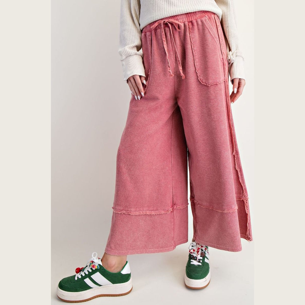 Mineral-washed pink palazzo pants with a drawstring waist and raw-edge seams, paired with green platform sneakers.