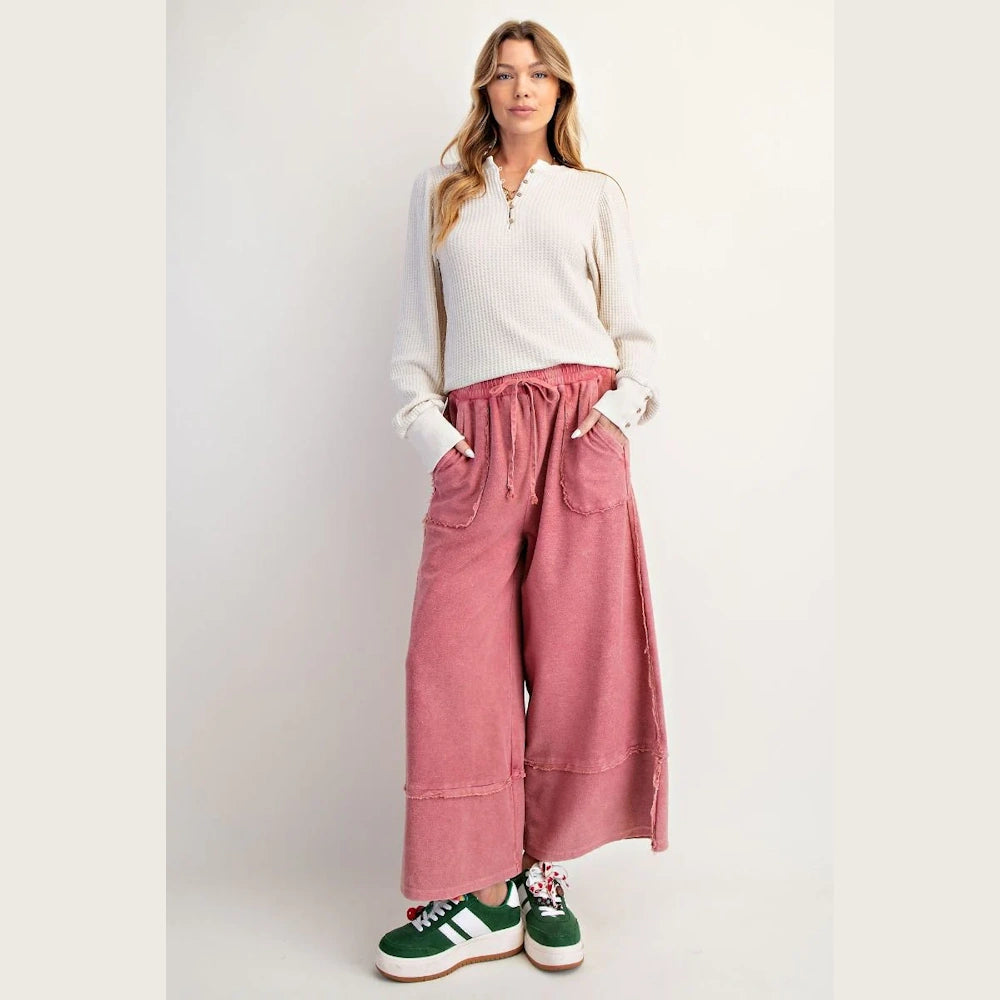 Woman wearing pink mineral washed palazzo pants and a white waffle knit henley shirt with green sneakers.