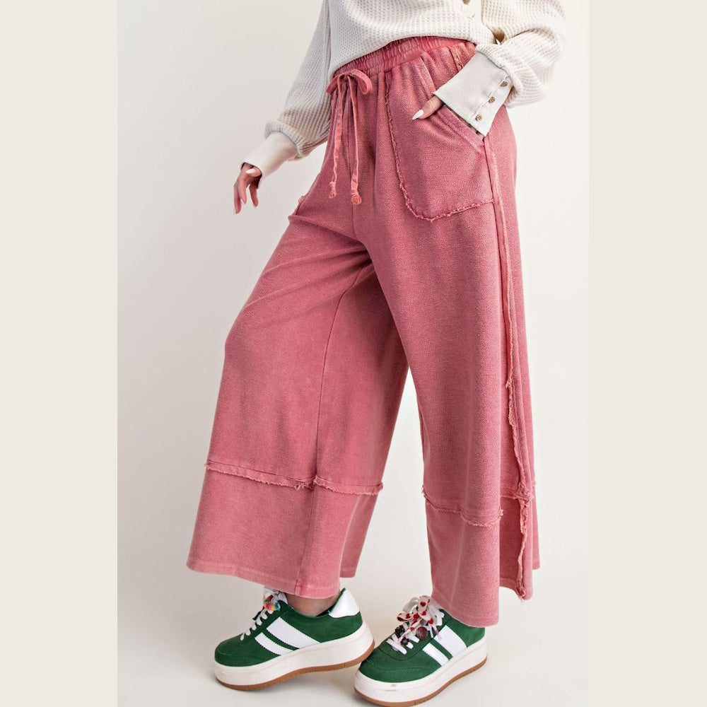 Woman wearing pink mineral washed wide-leg palazzo pants with raw hem detail and green sneakers.