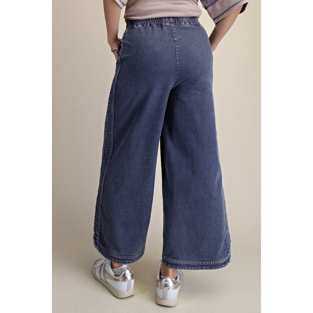 Back view of dark mineral-wash wide-leg denim pants featuring an elastic waistband and curved hems.