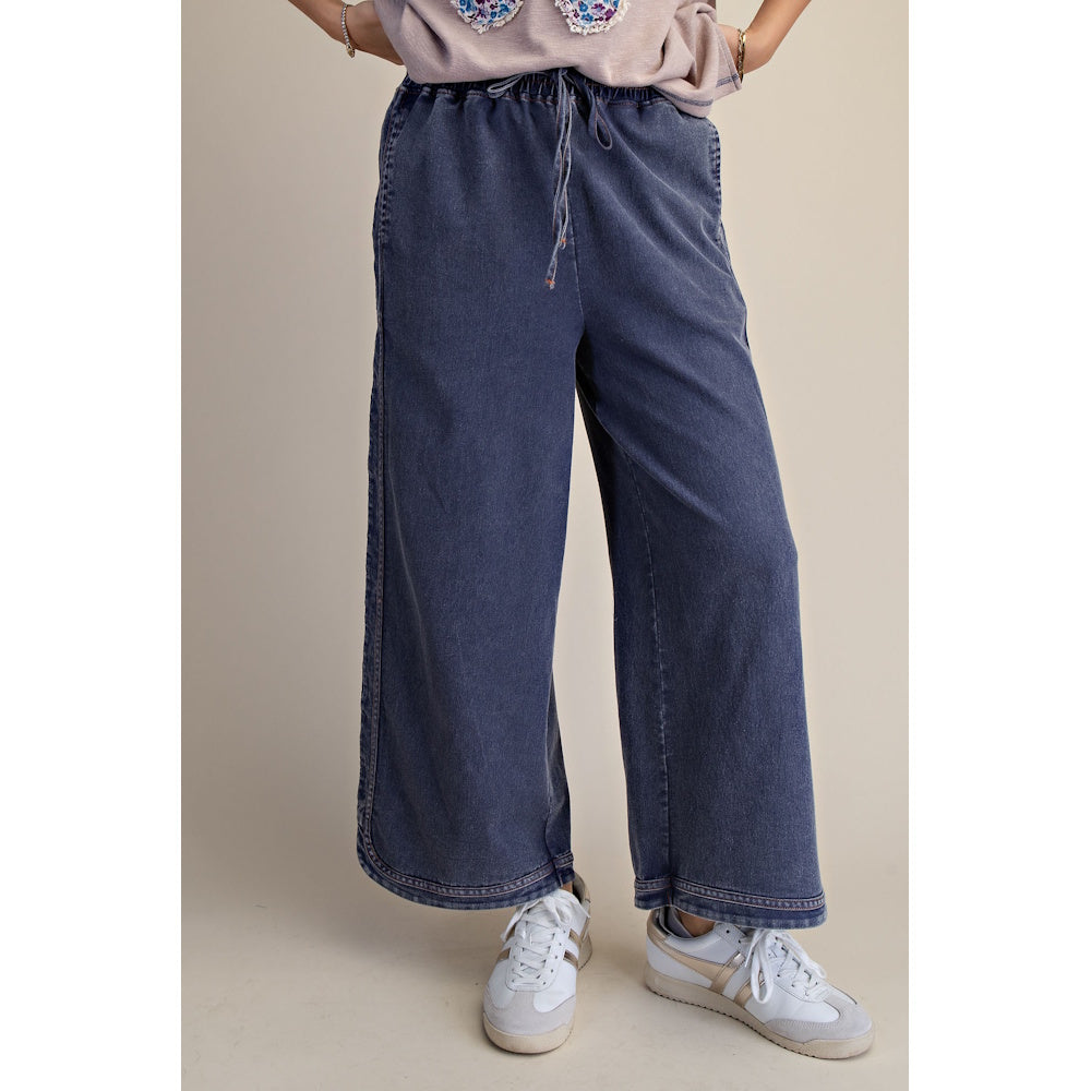 Mineral-washed dark denim wide-leg pants with an elastic drawstring waist paired with white sneakers.