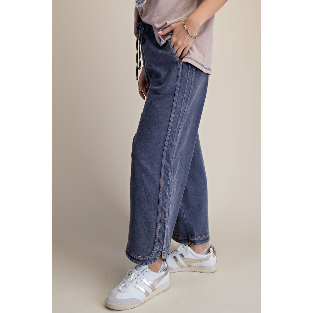 Side view of a person wearing dark mineral-washed denim drawstring pants with white sneakers.