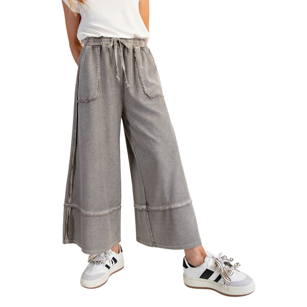 A person wearing grey, wide-leg mineral-washed jogger pants with a drawstring and white sneakers.