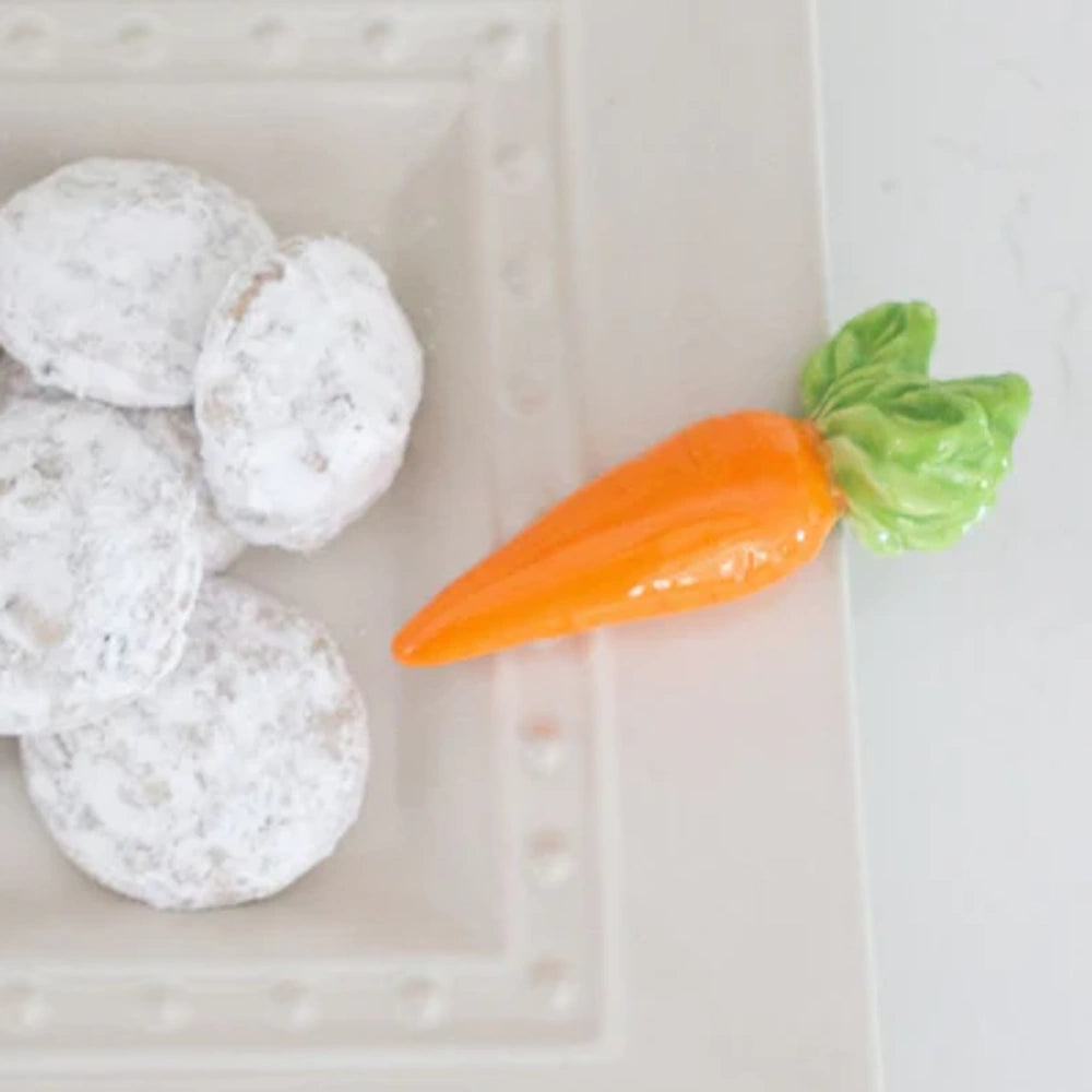 Powdered sugar cookies on a white plate with a decorative ceramic orange carrot.