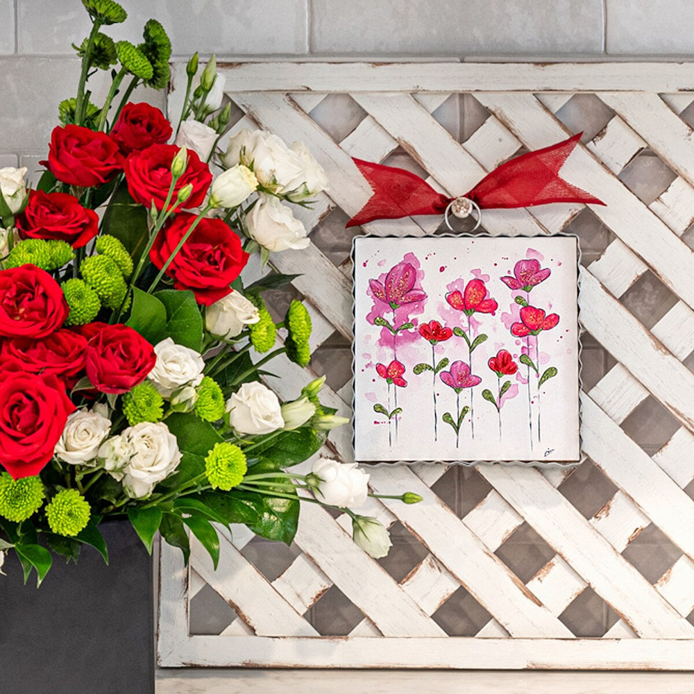 Pink floral wall art with red bow hanging on white lattice next to a bouquet of red and white roses.