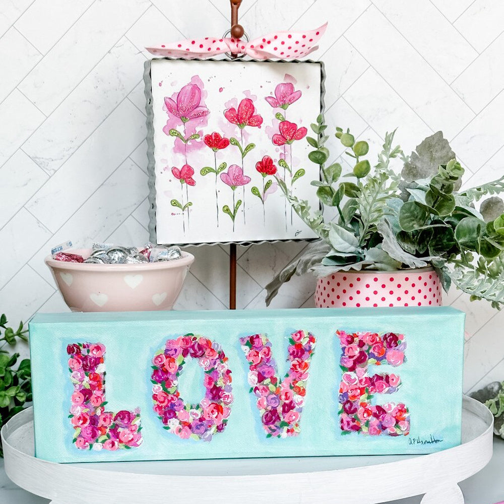 Floral LOVE canvas art and pink flower painting display with spring decor and greenery on a white tiered tray.