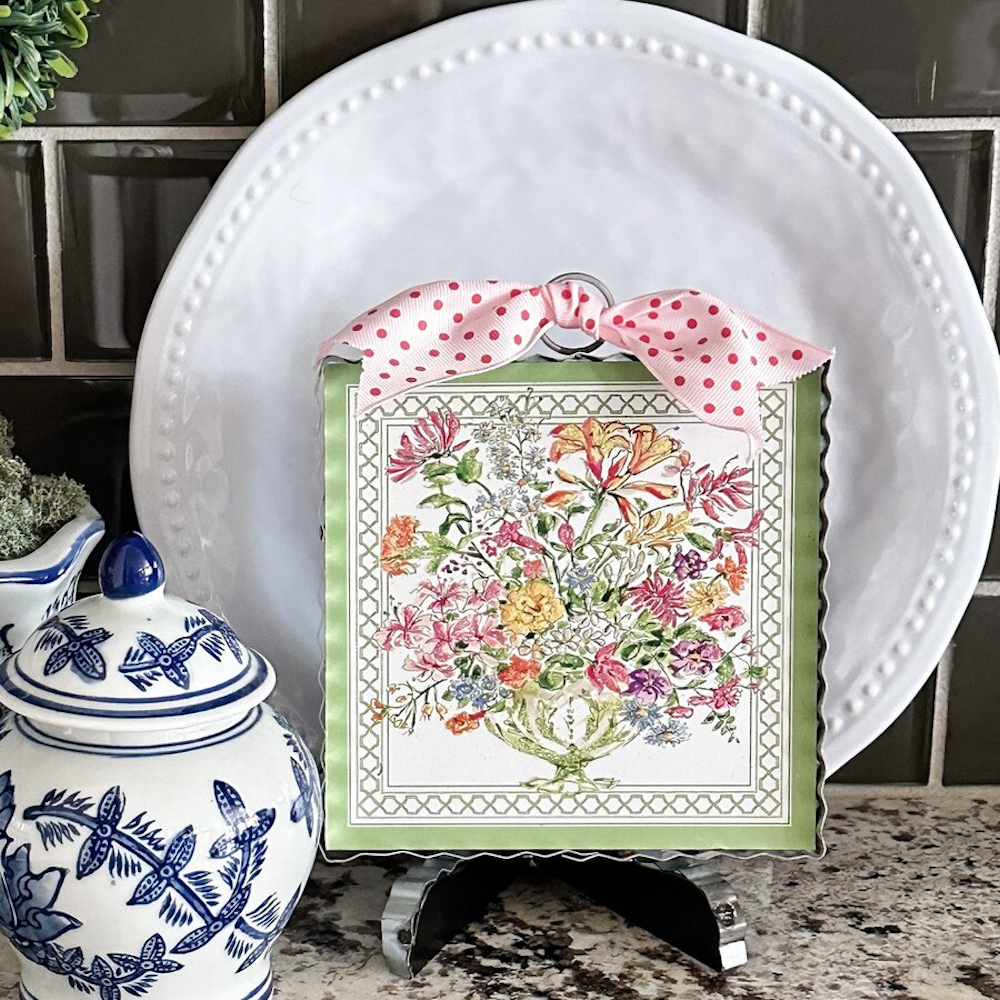 Watercolor floral arrangement mini art in a green frame with a pink polka dot bow, displayed on a kitchen counter.