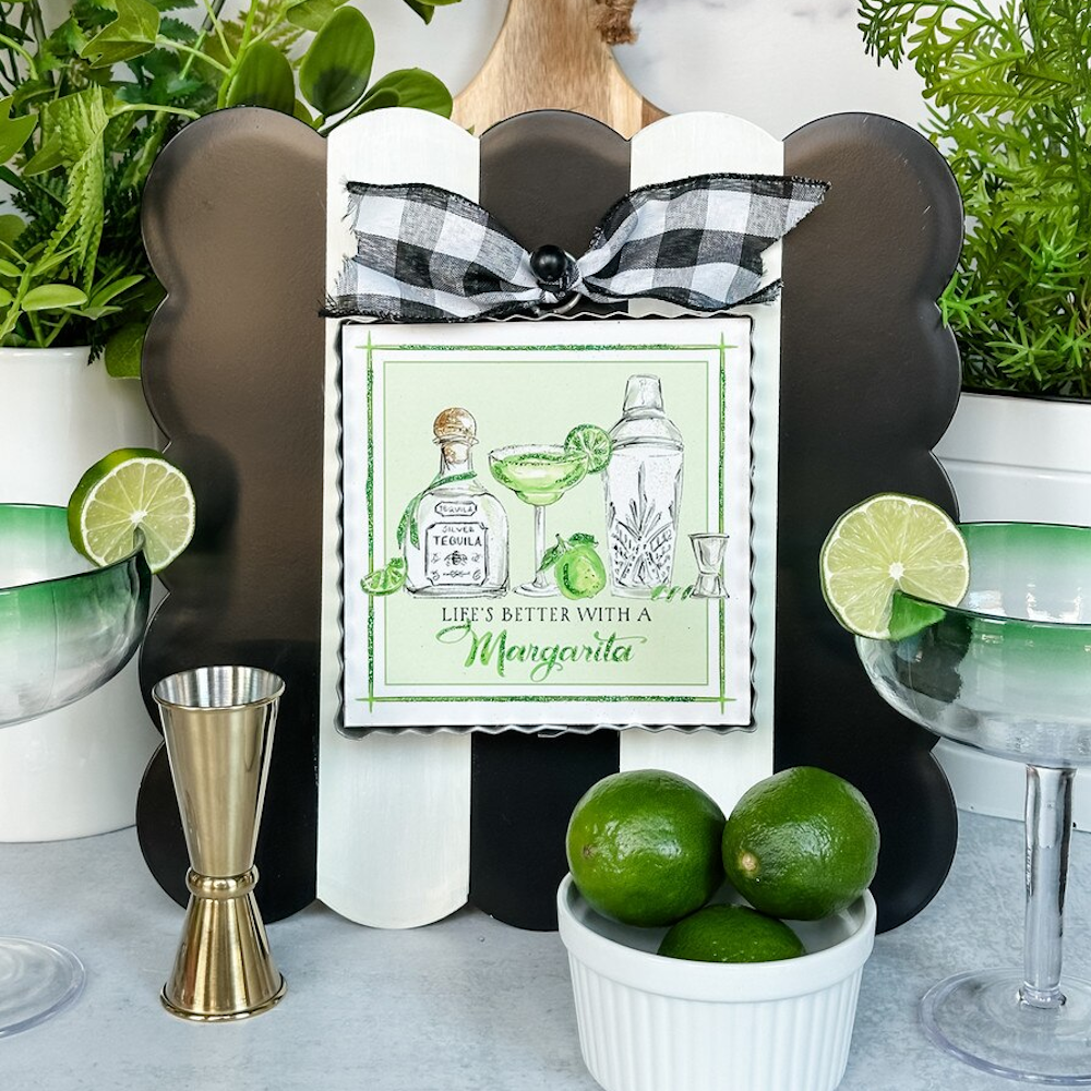 Margarita art sign with tequila, shaker, and limes on a black and white striped scalloped frame with a buffalo check bow.