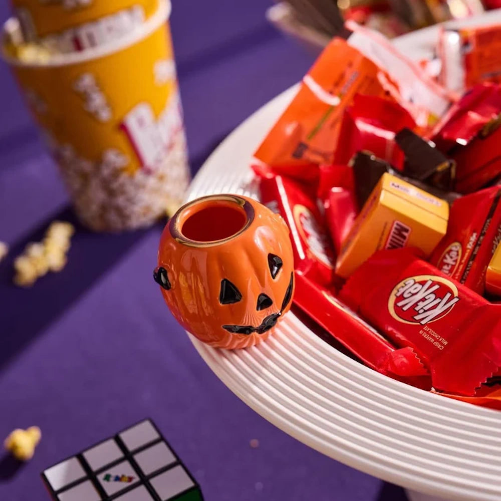 A small ceramic jack-o'-lantern decoration on the rim of a white platter filled with Halloween candy.