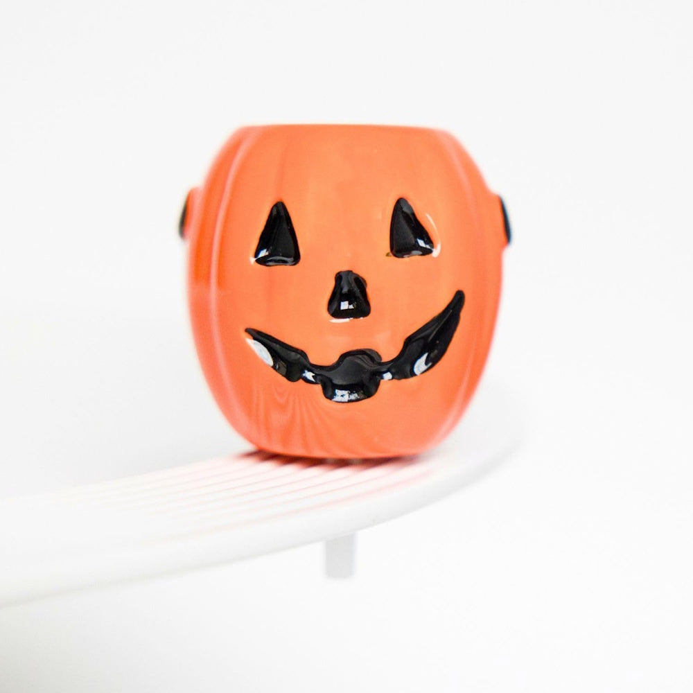 A small, glossy orange jack-o'-lantern decoration sitting on the rim of a white ceramic dish.