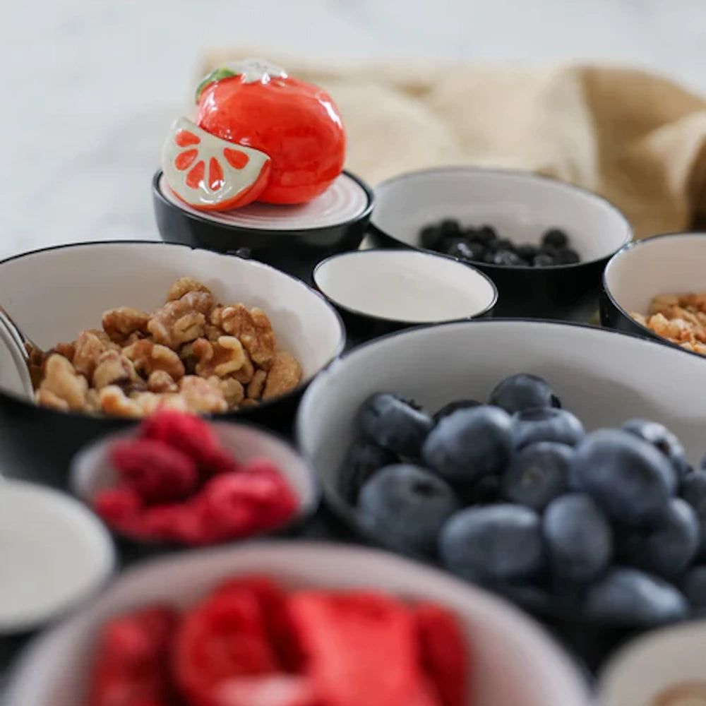 Bowls of blueberries, raspberries, walnuts, and a ceramic orange figurine on a white table.