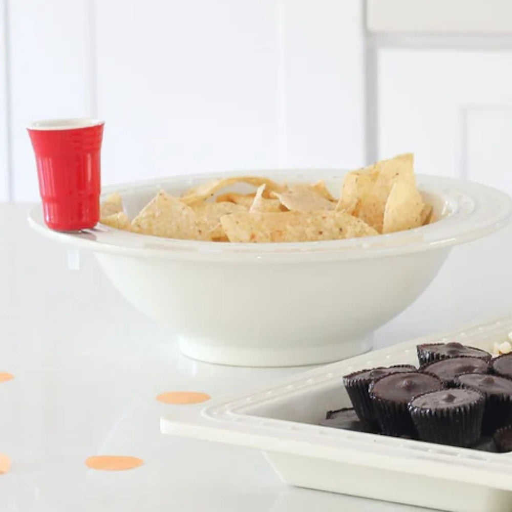 A small red party cup charm attached to a large white bowl filled with tortilla chips.