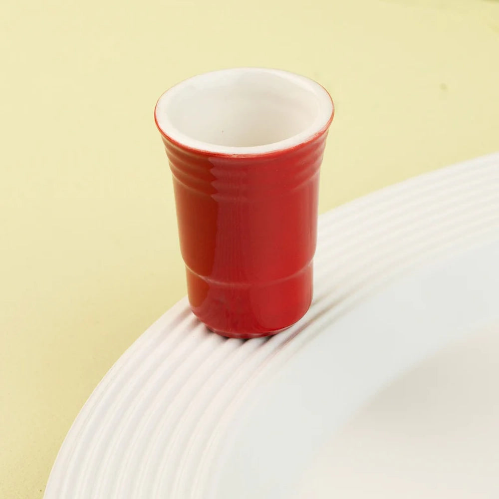 A miniature ceramic red party cup decoration attached to the rim of a white textured serving platter.