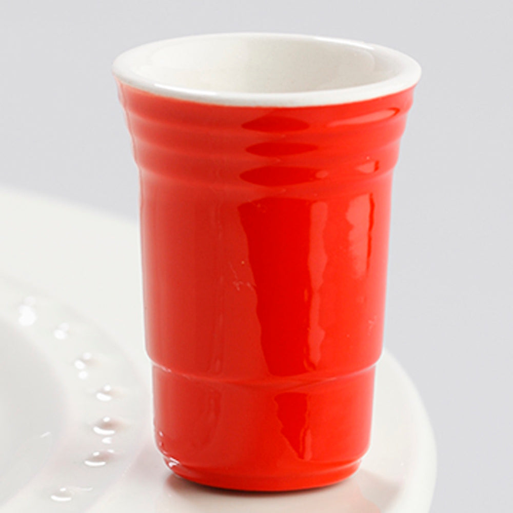 A small, glossy red ceramic cup shaped like a party cup, sitting on the edge of a white plate.