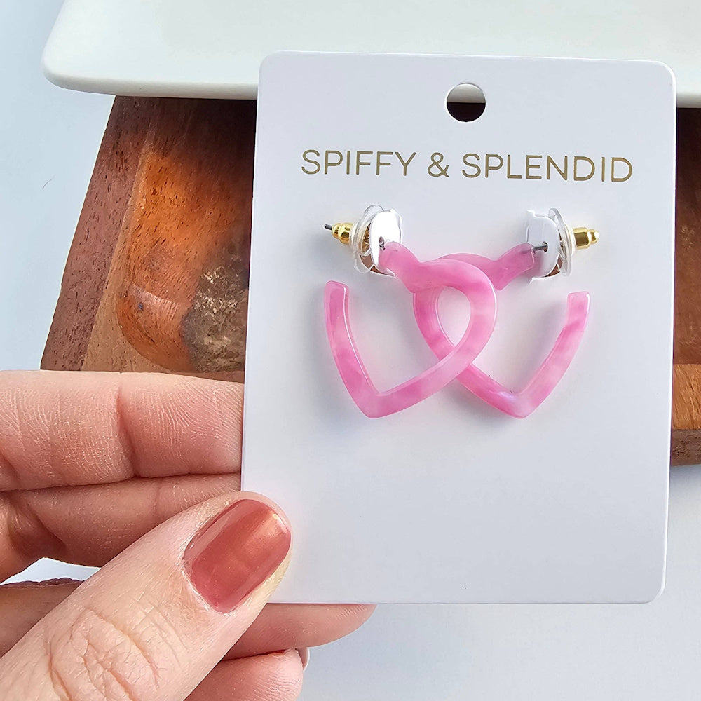 Spiffy & Splendid pink marble acetate mini heart hoop earrings on a white card held by a hand with pink nails.