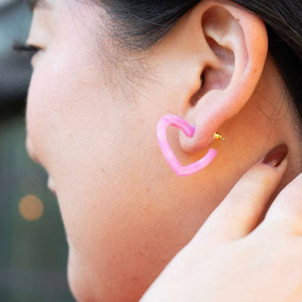 Woman wearing a pink bubblegum resin mini heart hoop earring. Close-up profile view of jewelry and ear piercing.