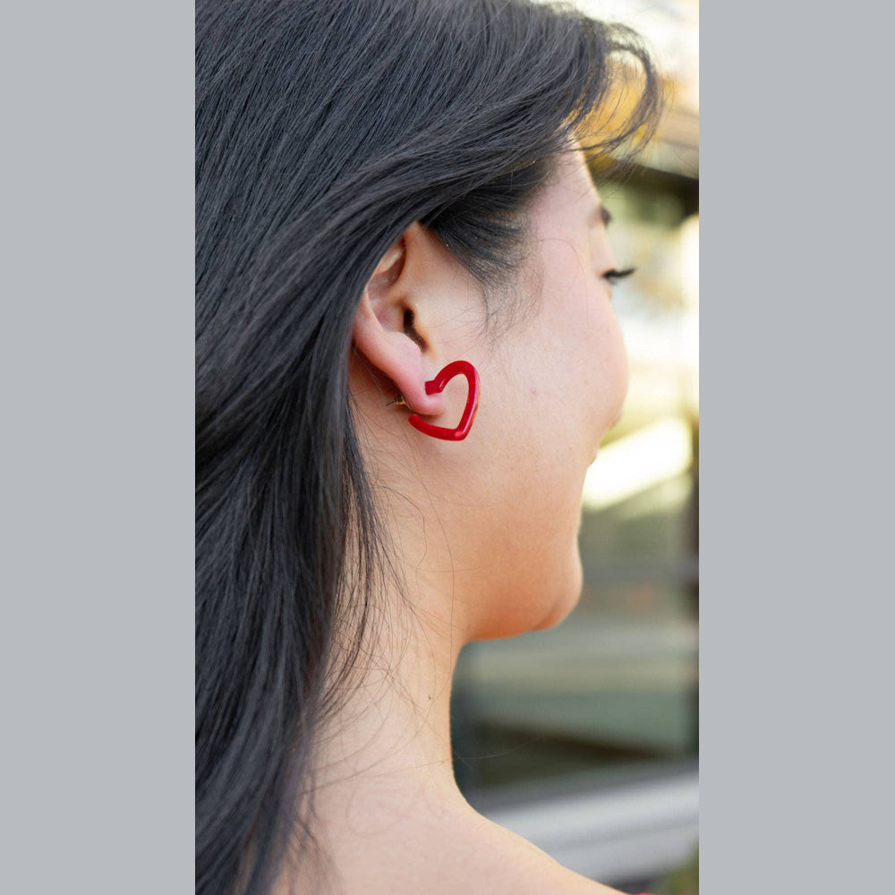 Woman wearing a small red heart-shaped hoop earring, profile view showing dark hair and jewelry detail.