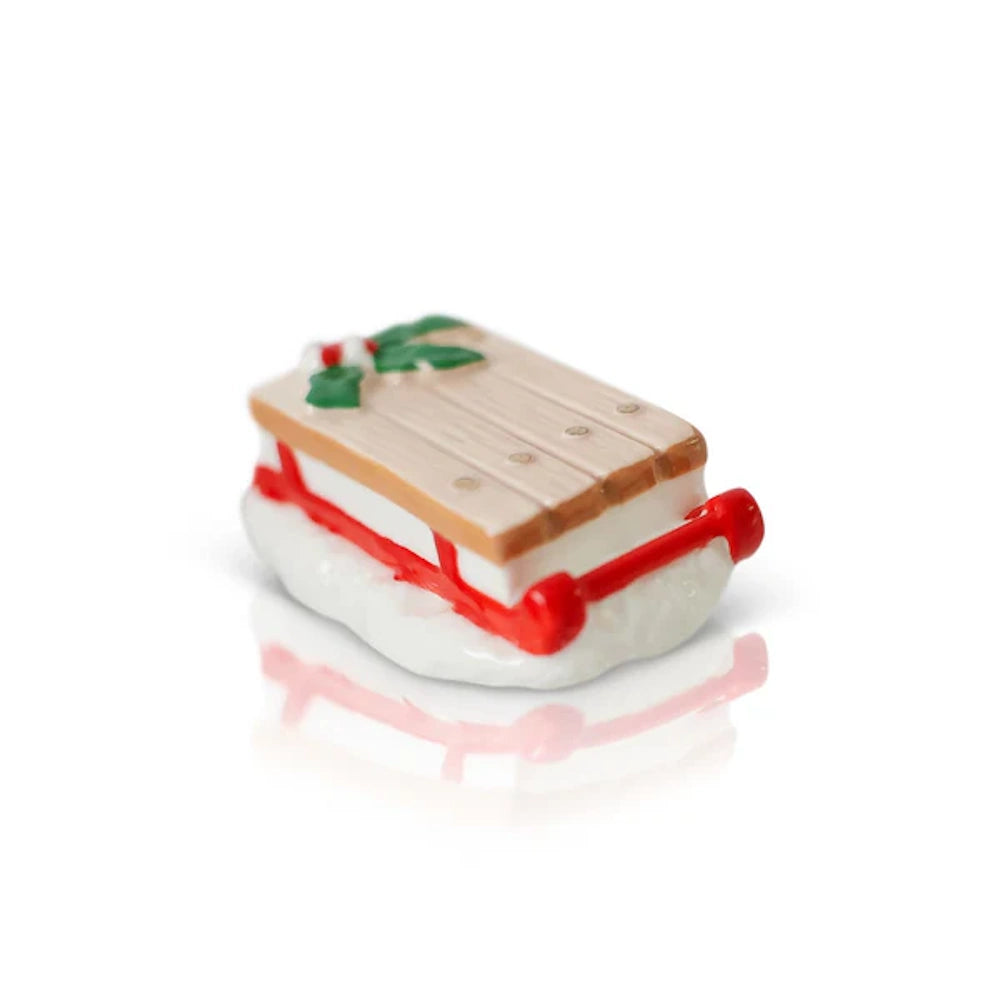 Miniature wooden Christmas sled with red runners and holly detail on a white snowy base.