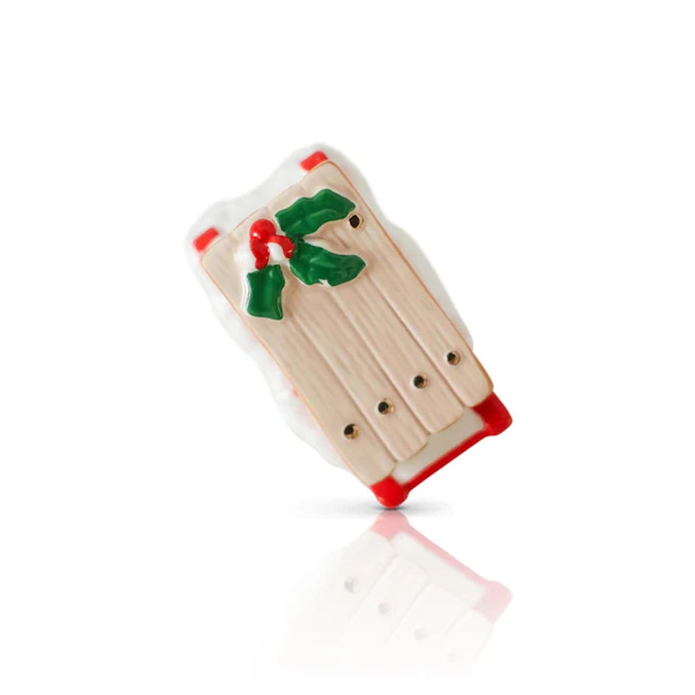 Wooden holiday sled charm with red runners, green holly leaves, and red berries on a white background.