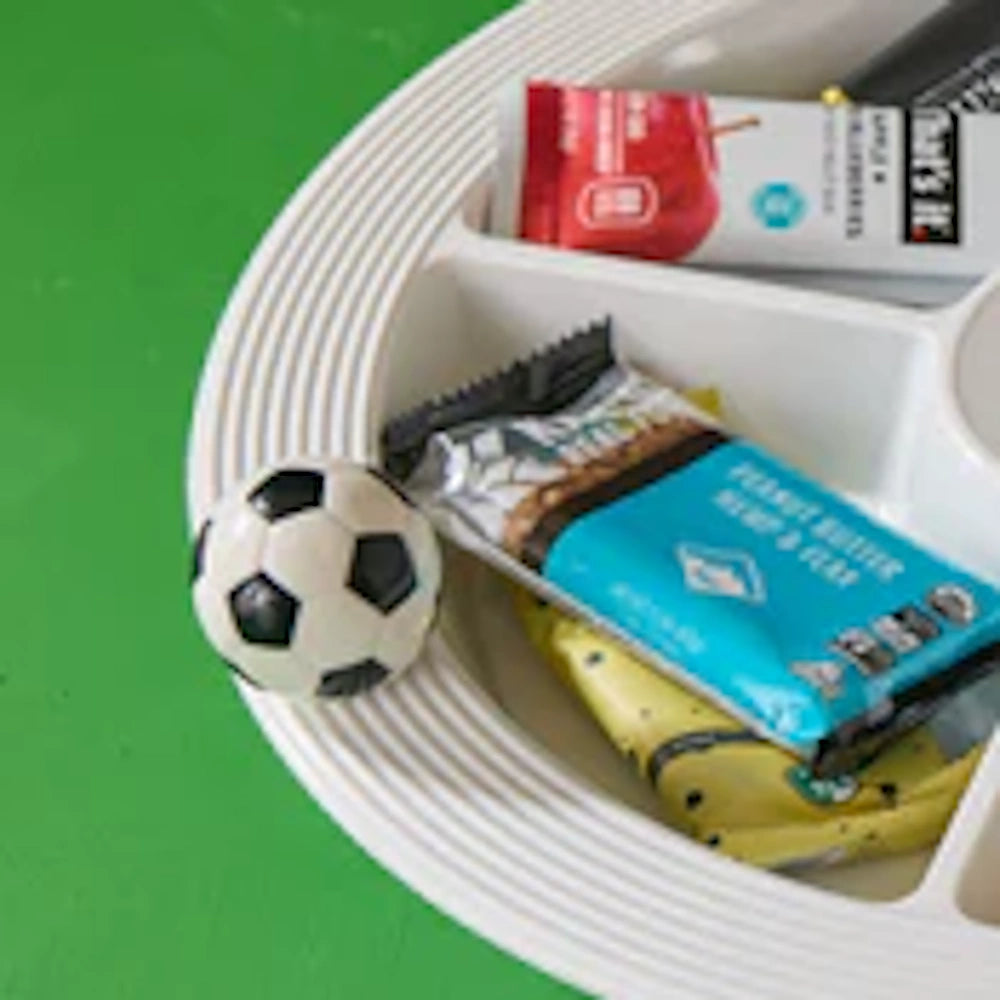 White divided snack tray filled with granola bars, featuring a small soccer ball charm on the rim.