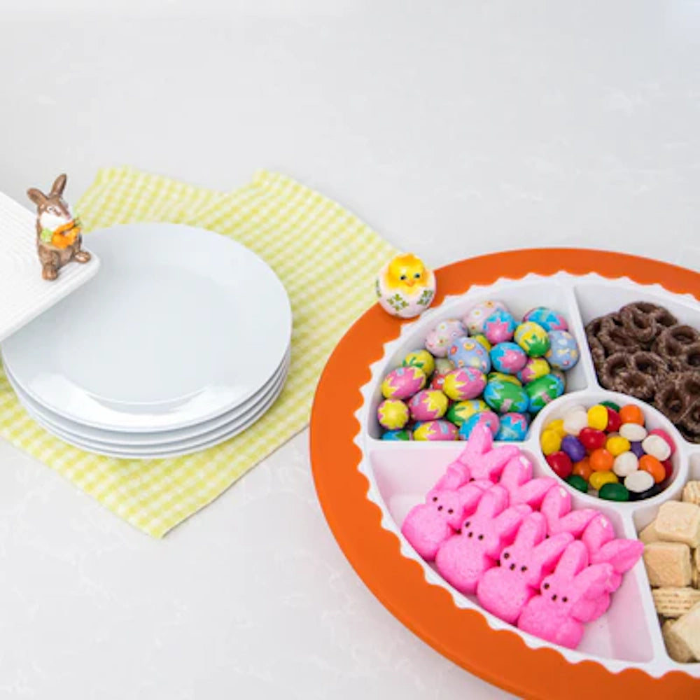 Easter candy platter with Peeps, jelly beans, and chocolate pretzels next to white plates and a yellow gingham napkin.