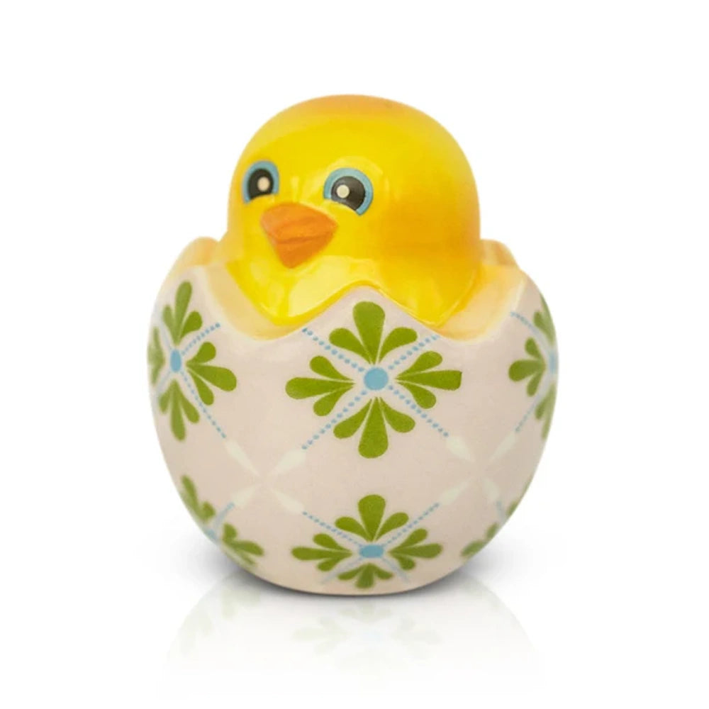 Yellow ceramic chick figurine inside a decorative cracked eggshell with green floral patterns on a white surface.