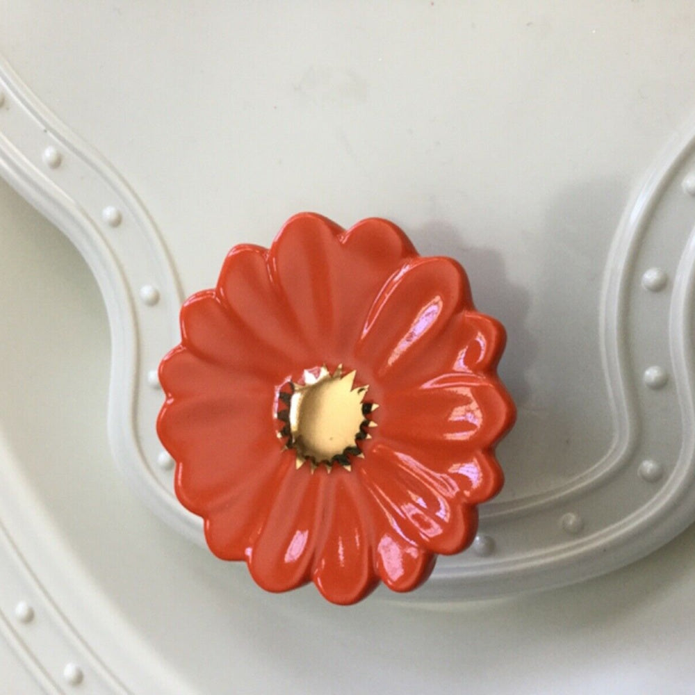 Mini orange gerbera daisy ceramic attachment with a shiny gold center attached to a white dish.