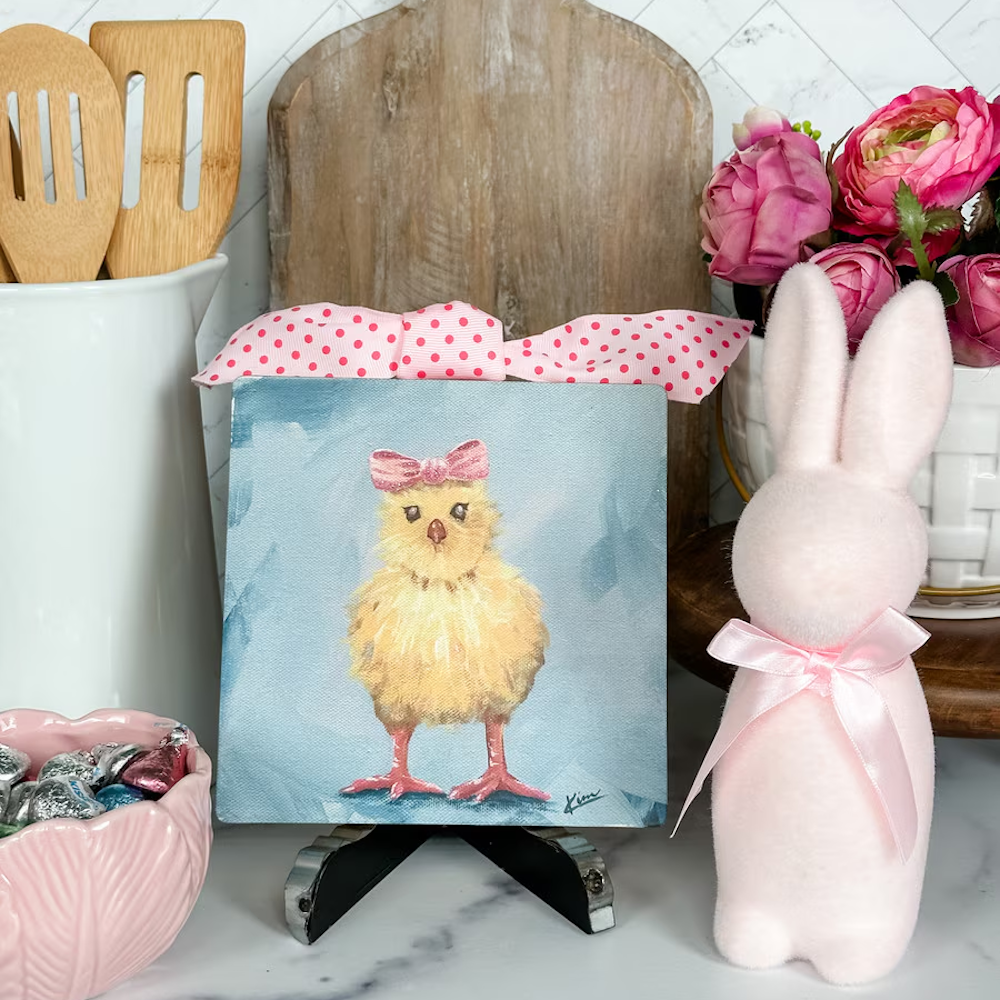 Hand-painted yellow chick art with a pink polka dot bow, displayed next to a pink bunny figurine for spring decor.