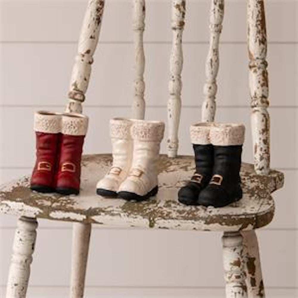 Three pairs of mini Santa boot vases in red, white, and black displayed on a distressed wooden chair.