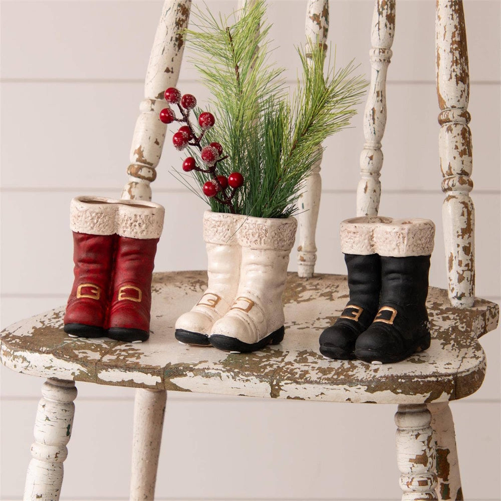 Three pairs of mini Santa boot vases in red, white, and black on a distressed chair.