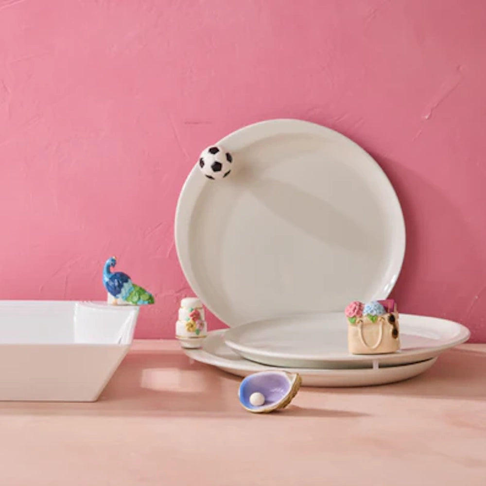 White ceramic plates and a bowl decorated with small soccer ball and peacock charms on a pink background.