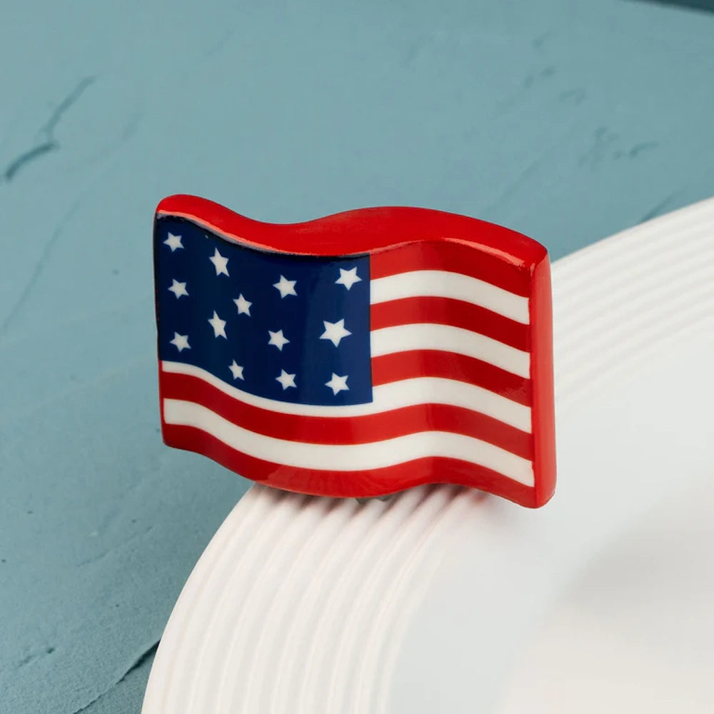A small, waving American flag decorative piece attached to the rim of a white ceramic plate.