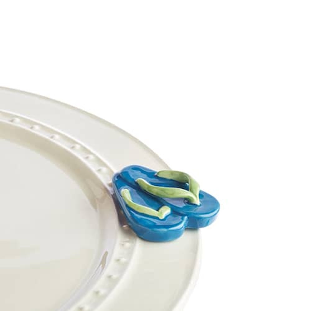 A small blue flip-flop charm attached to the rim of a white ceramic plate.