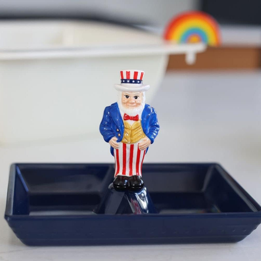 A small Uncle Sam figurine standing in a dark blue tray with a blurred rainbow in the background.