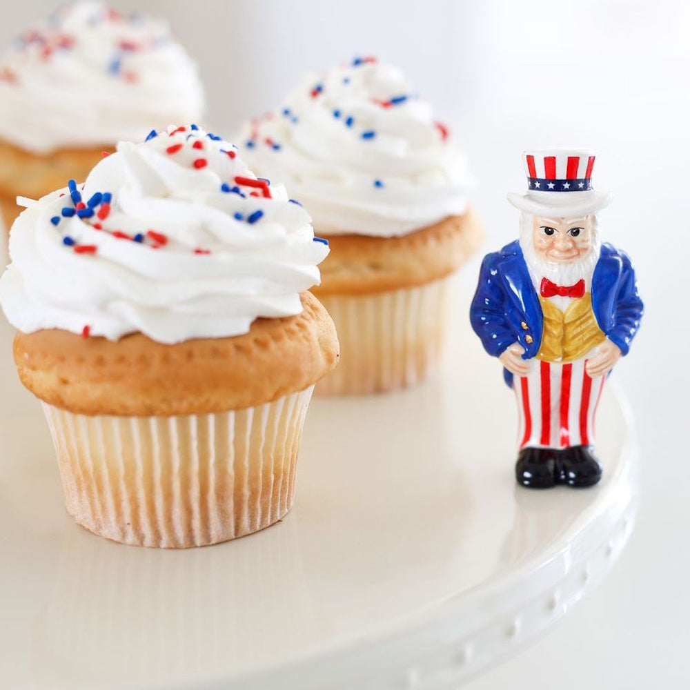 Vanilla cupcakes with white frosting and red and blue sprinkles next to a small Uncle Sam figurine.