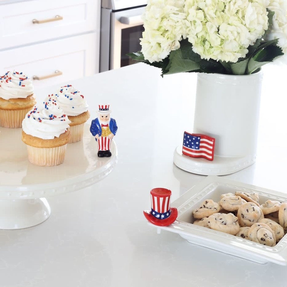 Patriotic kitchen display with cupcakes, cookies, white flowers, and Uncle Sam themed ceramic decorations.