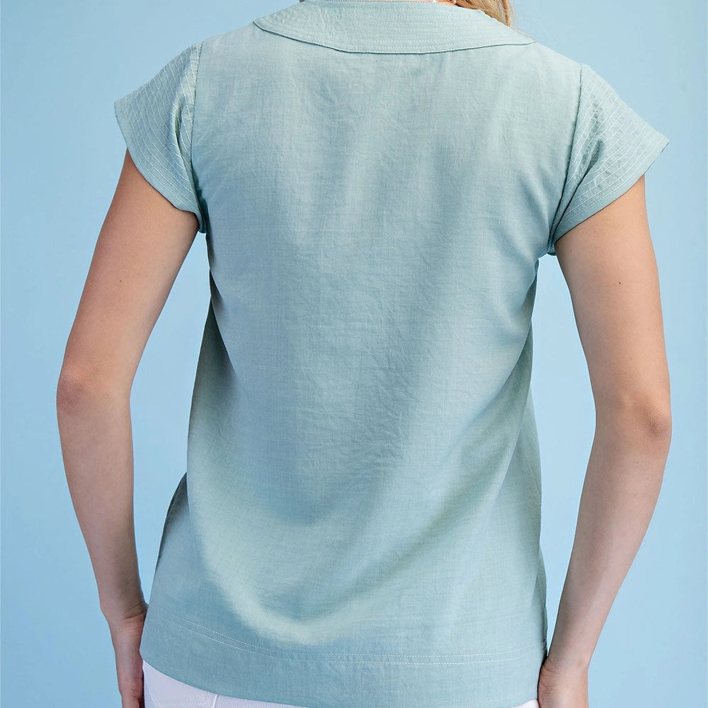 Back view of a woman wearing a mint V-neck blouse with trapunto-stitched cap sleeves and a relaxed fit.