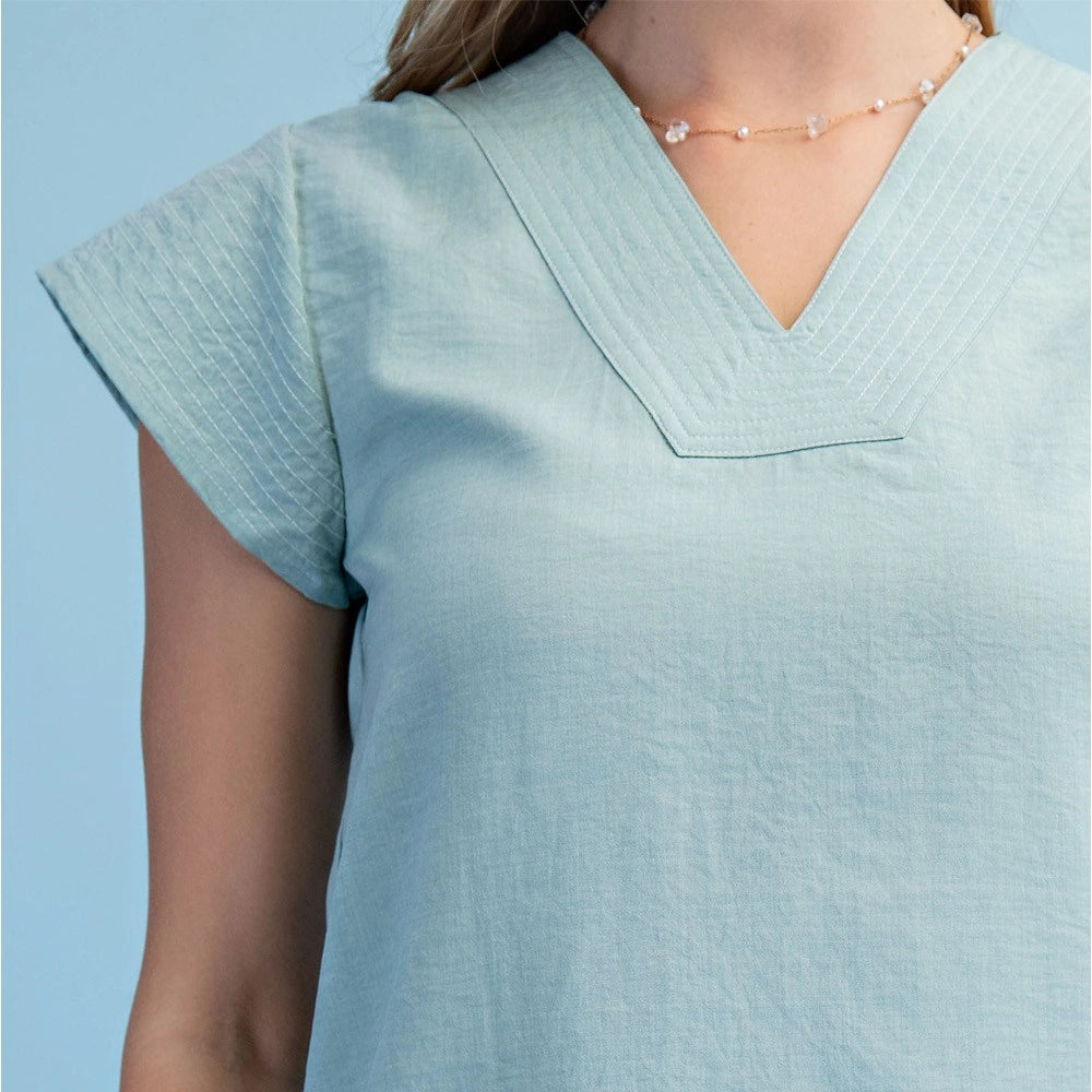 Close-up of a mint V-neck blouse featuring trapunto stitching on the neckline and loose cap sleeves.