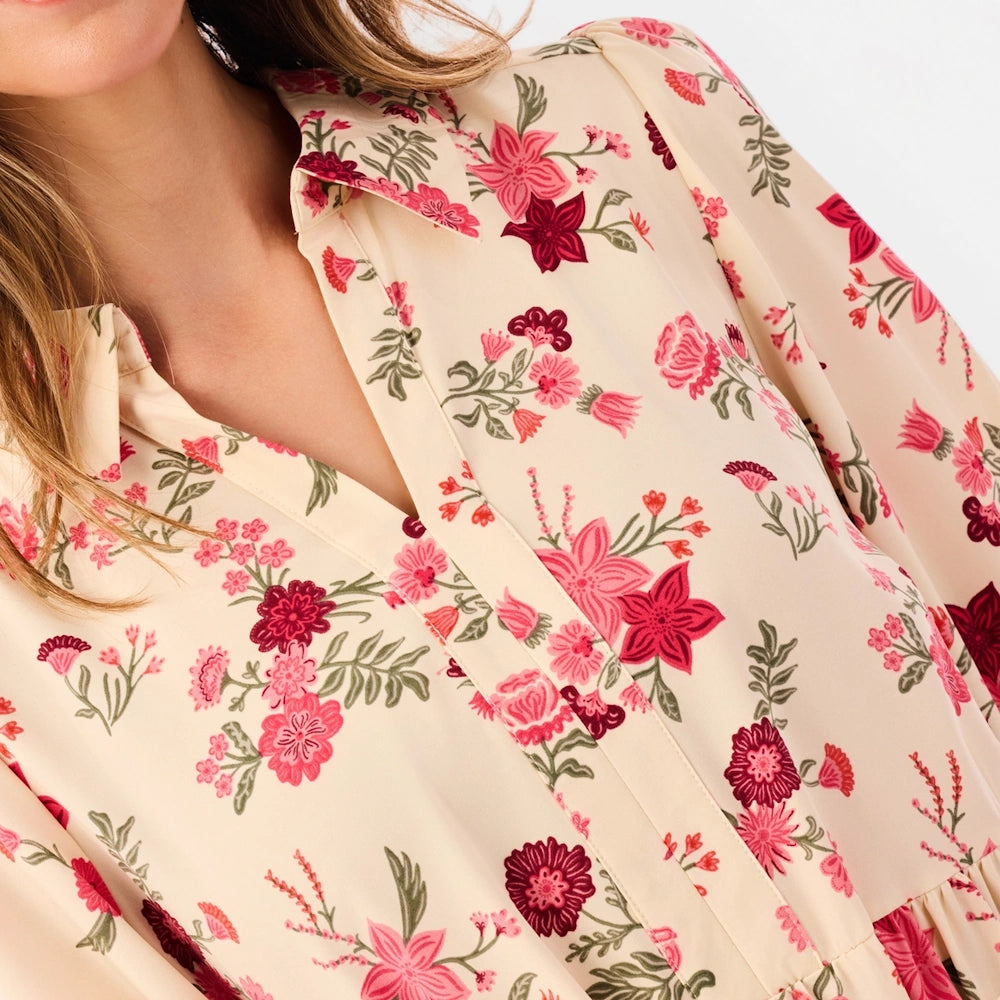 Close-up of a cream floral shirt dress showing a collared V-neckline and pink flower pattern.