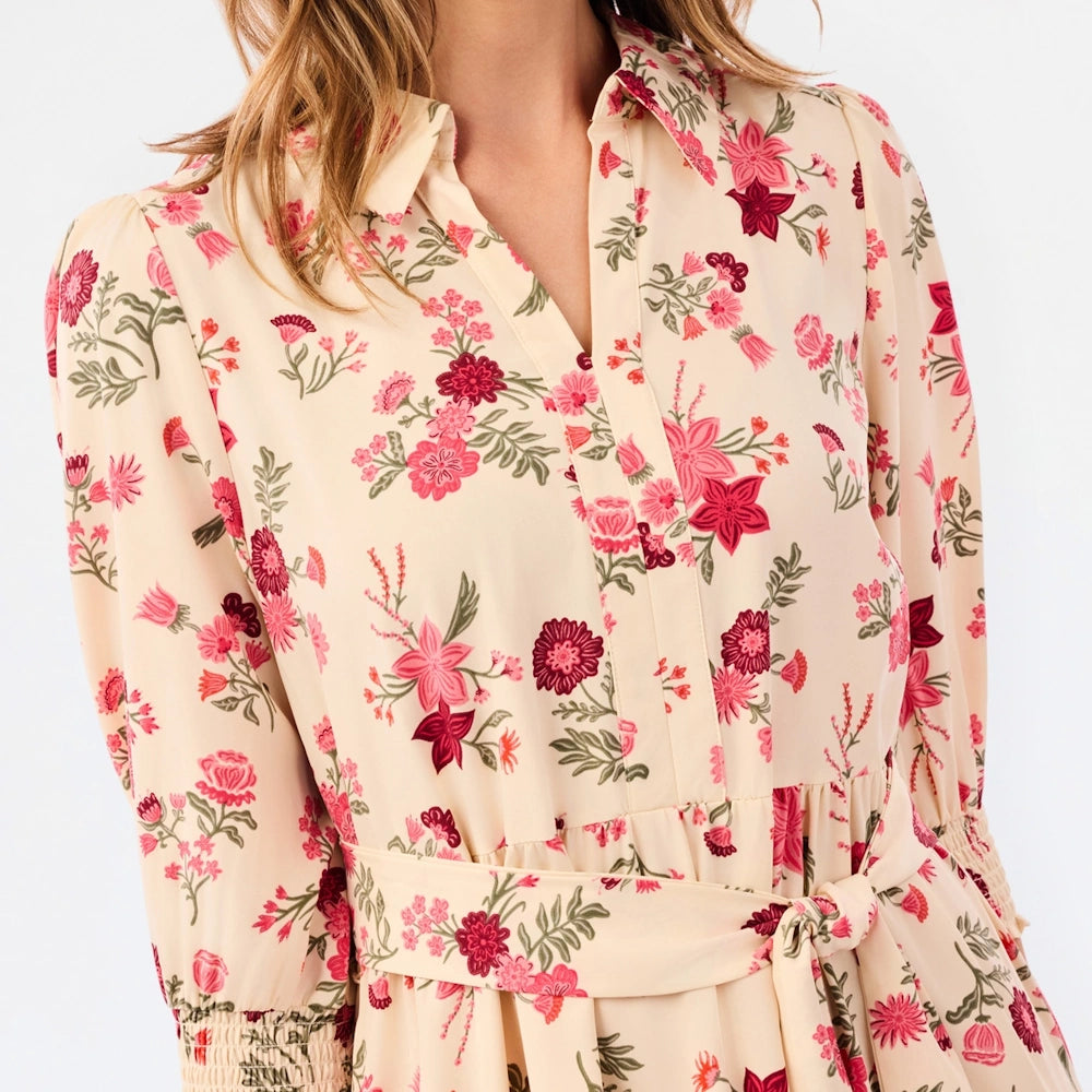 Front detail of a cream floral dress featuring a collared V-neckline, tie waist, and smocked cuffs.