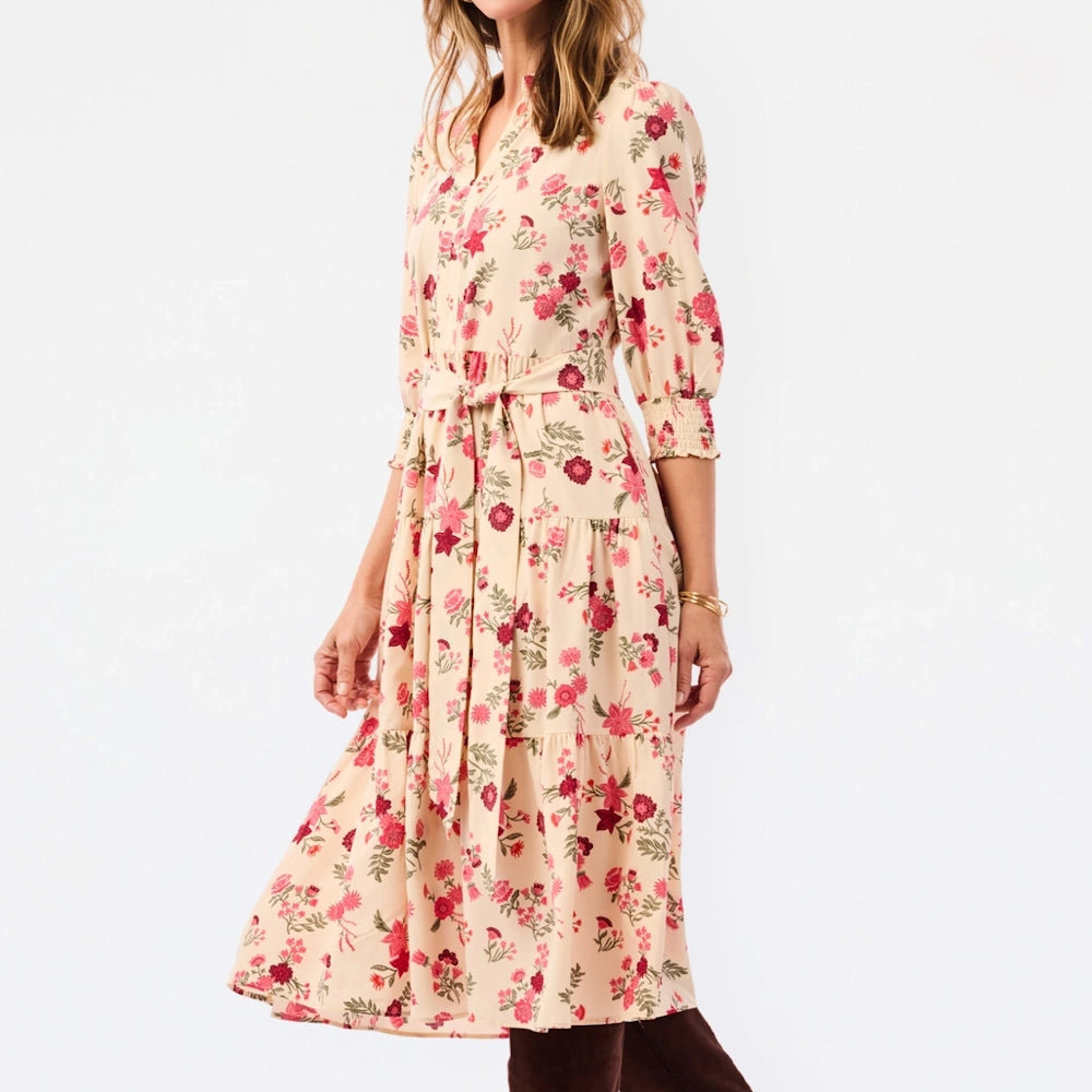 Side view of cream tiered midi dress in pink floral print with tie waist belt and three-quarter sleeves.