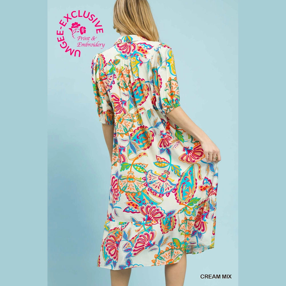 Woman in a cream maxi dress with a colorful mixed paisley print and puff sleeves, shown from the back against a blue background.