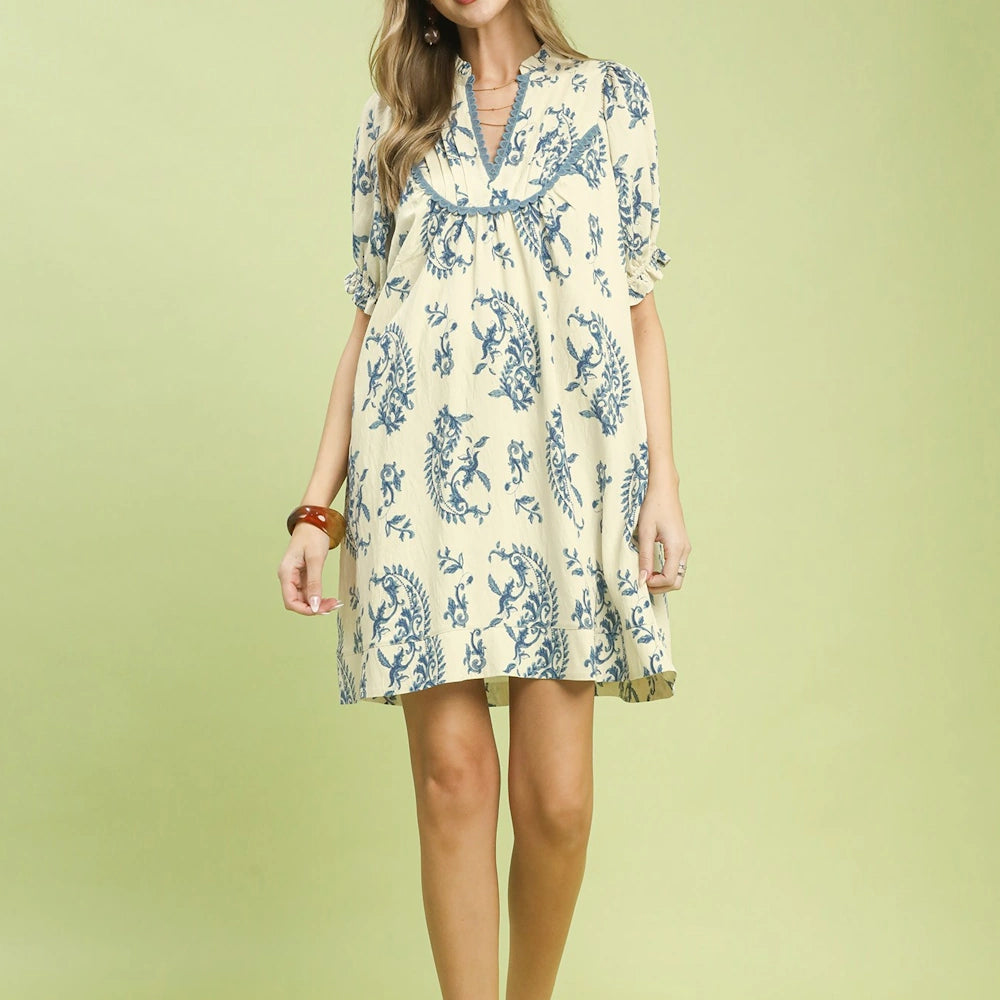 Cream short-sleeve mini dress with blue paisley print, V-neckline, and scalloped trim detailing.