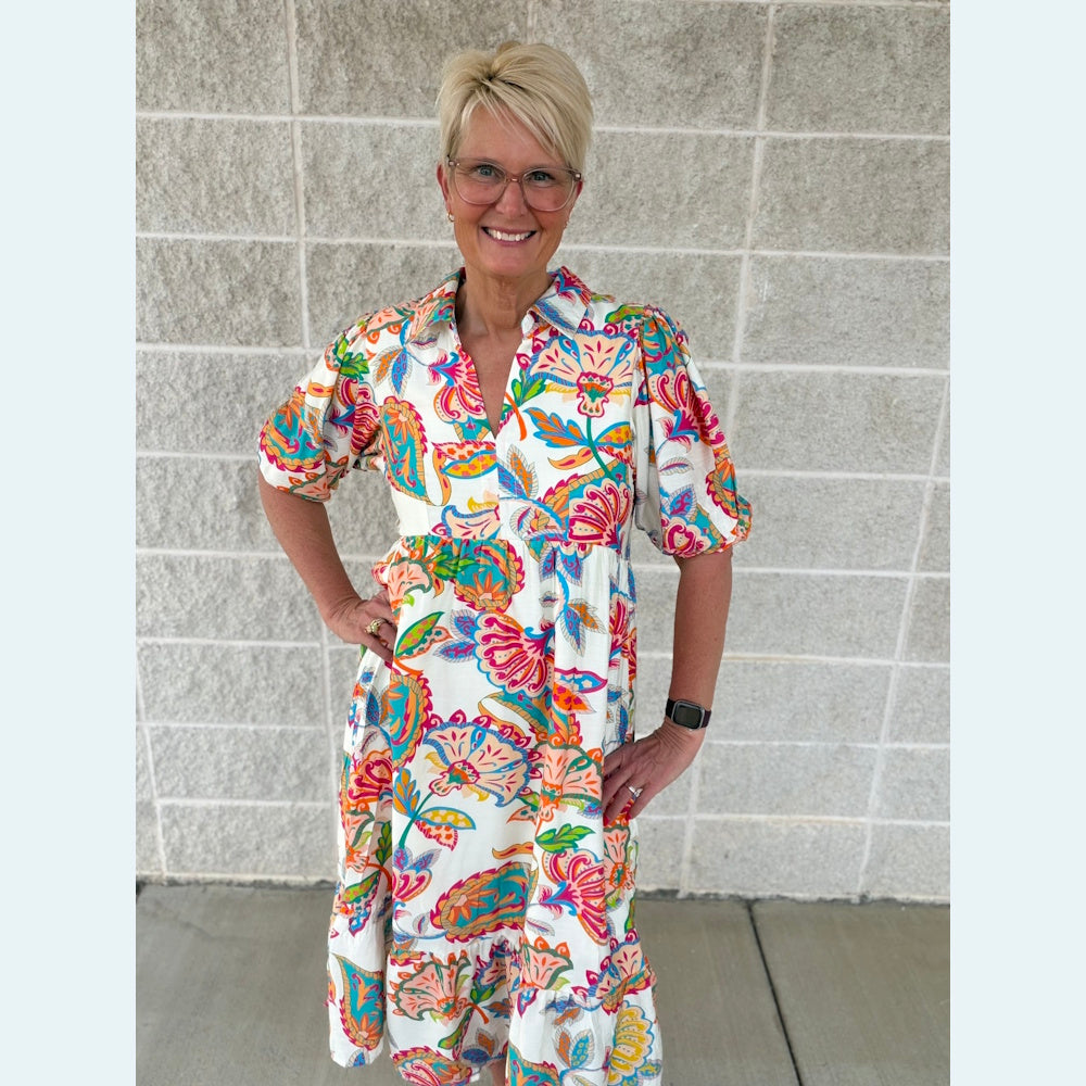 Smiling woman in a colorful mixed paisley print maxi dress with a collar and puff sleeves.