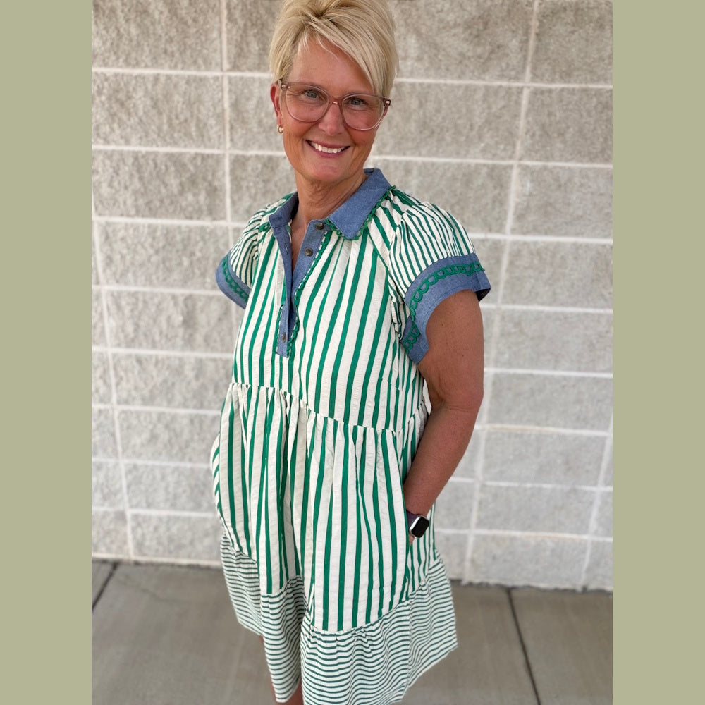 Smiling woman in a green and white striped, tiered babydoll dress with blue denim trim.
